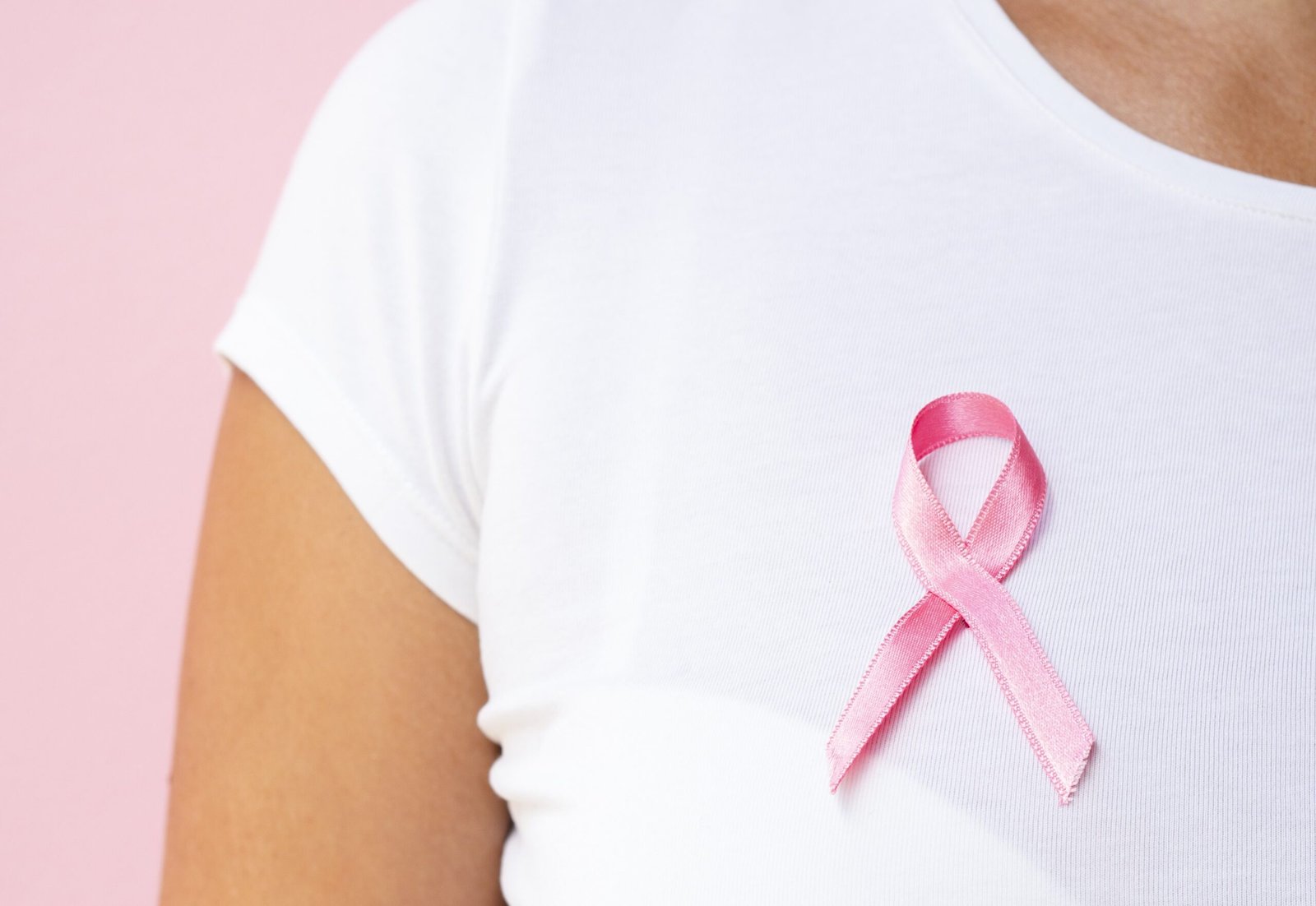 Fita que é símbolo do outubro rosa preso numa camisa vestida por uma mulher